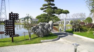 A pathway leading to a pond with directional signs, a large rock formation, and a well-maintained lawn.