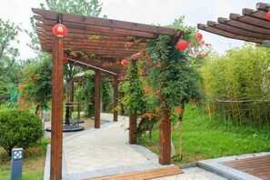 Una estructura de pérgola de madera con plantas trepadoras y flores rojas, un sendero empedrado y un jardín con diversas plantas.
