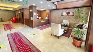 Un'area della reception di un hotel con una scrivania, una poltrona rossa, un divano e una pianta in vaso.