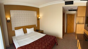 Una camera d'albergo con un letto, abat-jour, una testiera in legno, una coperta a motivi e un armadio.