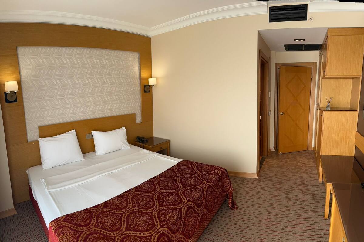 A hotel room with a bed, bedside lamps, a wooden headboard, a patterned bedspread, and a wardrobe.