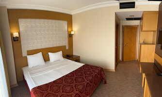 A hotel room with a bed, bedside lamps, a wooden headboard, a patterned bedspread, and a wardrobe.