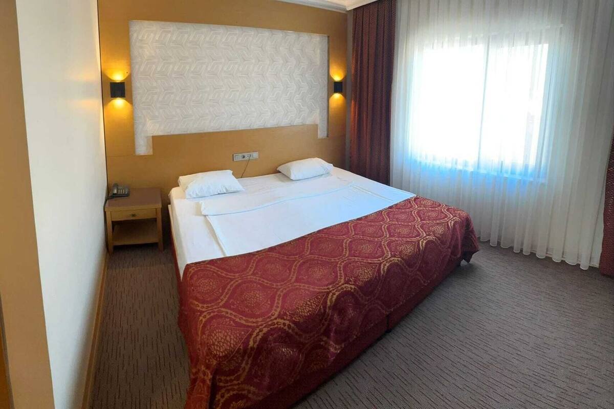 A hotel room with a large bed, a bedside table, and a window with curtains.