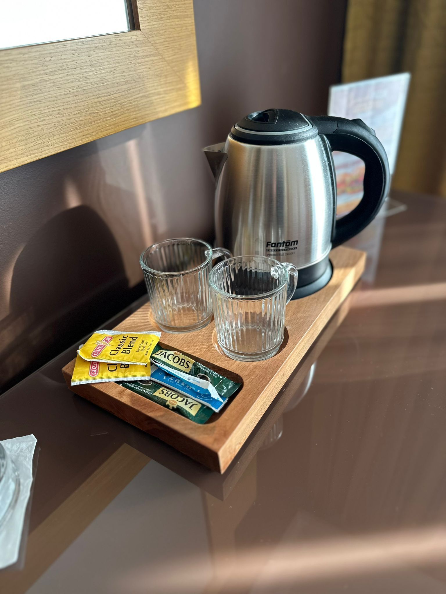Una bandeja de madera con una tetera, dos vasos pequeños y sobres de leche para café sobre una mesa.