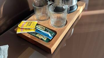Una bandeja de madera con una tetera, dos vasos pequeños y sobres de leche para café sobre una mesa.