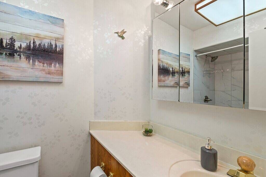 Un baño con tocador blanco, un espejo grande y un cuadro de un paisaje.