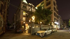 A nighttime street view with a building featuring a gated entrance and parked cars. - Xiaoshu Wushe Boutique Hostel (Haikou)