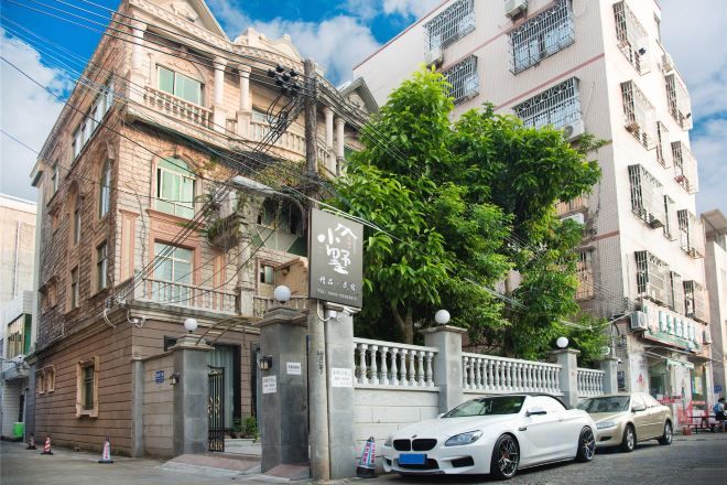 A multi-story building with a gated entrance, parked cars, and a tree in front.