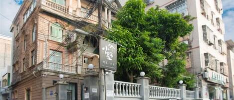 Un edificio de varios pisos con entrada porticada, coches aparcados y un árbol al frente.