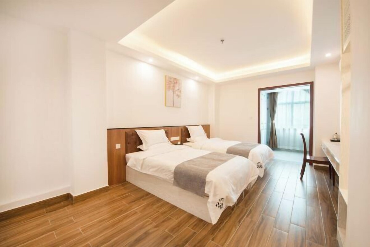 Une chambre d’hôtel avec deux lits, un plancher en bois, un luminaire au plafond et une fenêtre avec des rideaux.