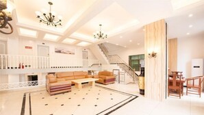 A spacious lobby with a high ceiling, a staircase, a seating area with sofas and a coffee table, and a reception desk. - Xiaoshu Wushe Boutique Hostel (Haikou)