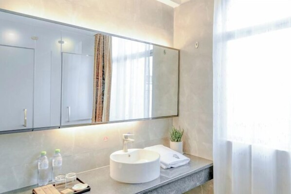Une salle de bain moderne avec un grand miroir, un lavabo rond et un plan de toilette où sont posés les articles de toilette.