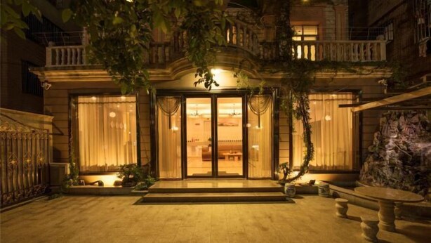 A well-lit entrance with a grand archway, a stone bench, and a small garden area. - Xiaoshu Wushe Boutique Hostel (Haikou)
