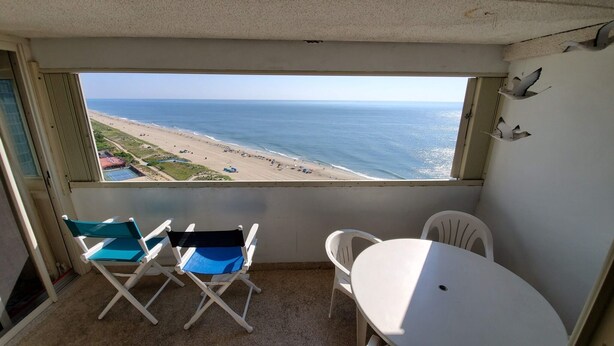 Un balcón con vista a la playa y al océano. Hay dos sillas plegables y una mesita.