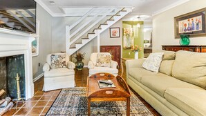 Una sala de estar con escaleras, una chimenea y una pared verde con un cuadro floral.