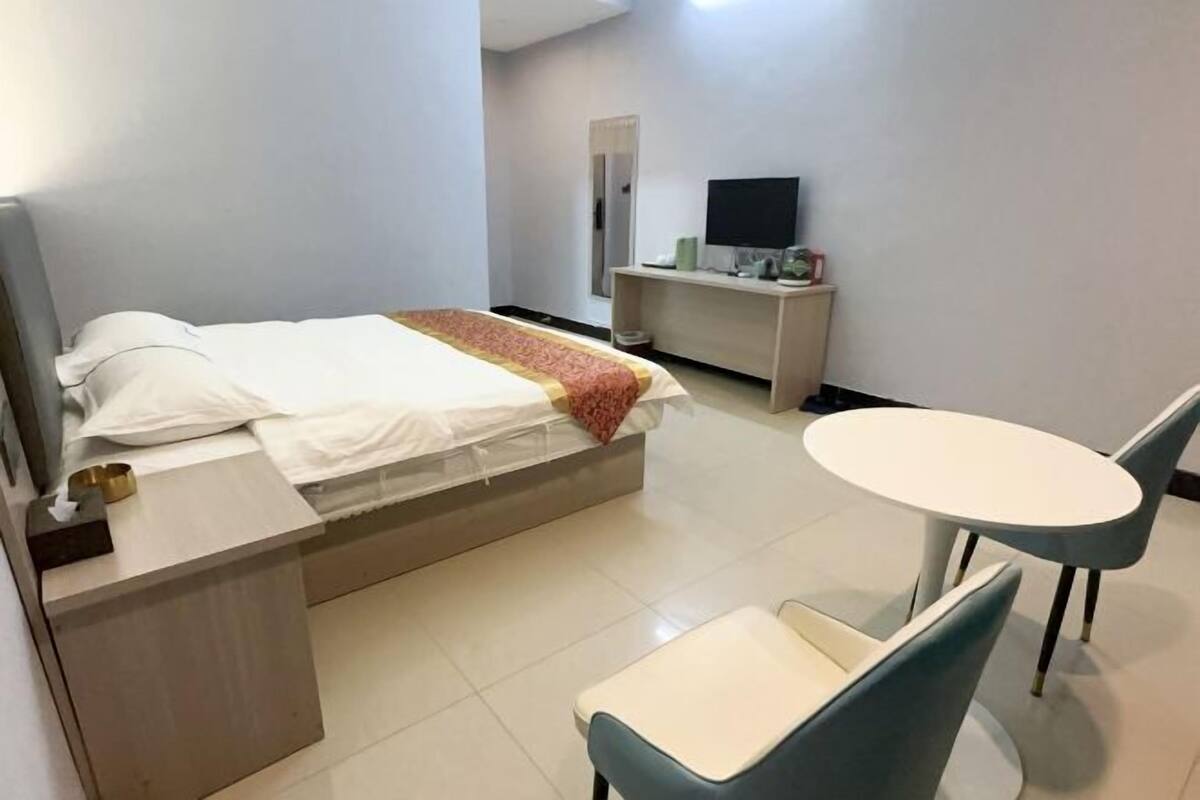 A hotel room with a bed, bedside table, chair, and a small round table.