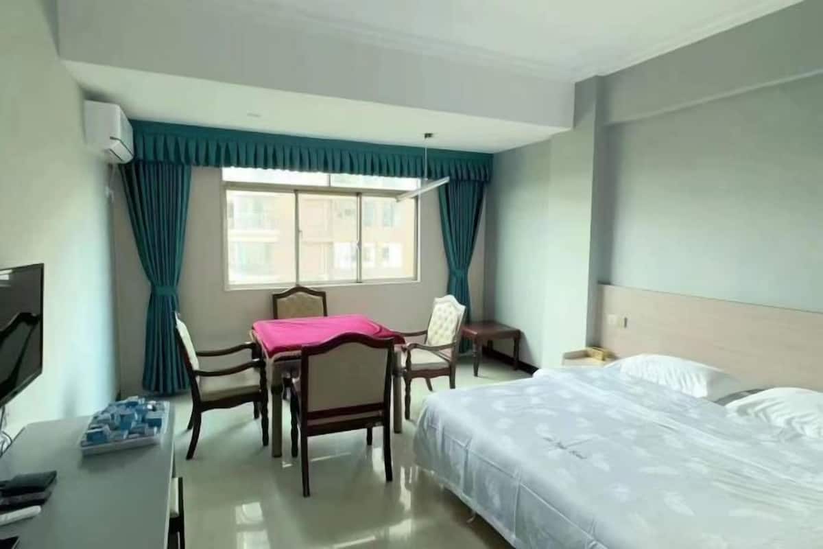 A hotel room with a bed, a desk with a chair, a TV, and a window with curtains.