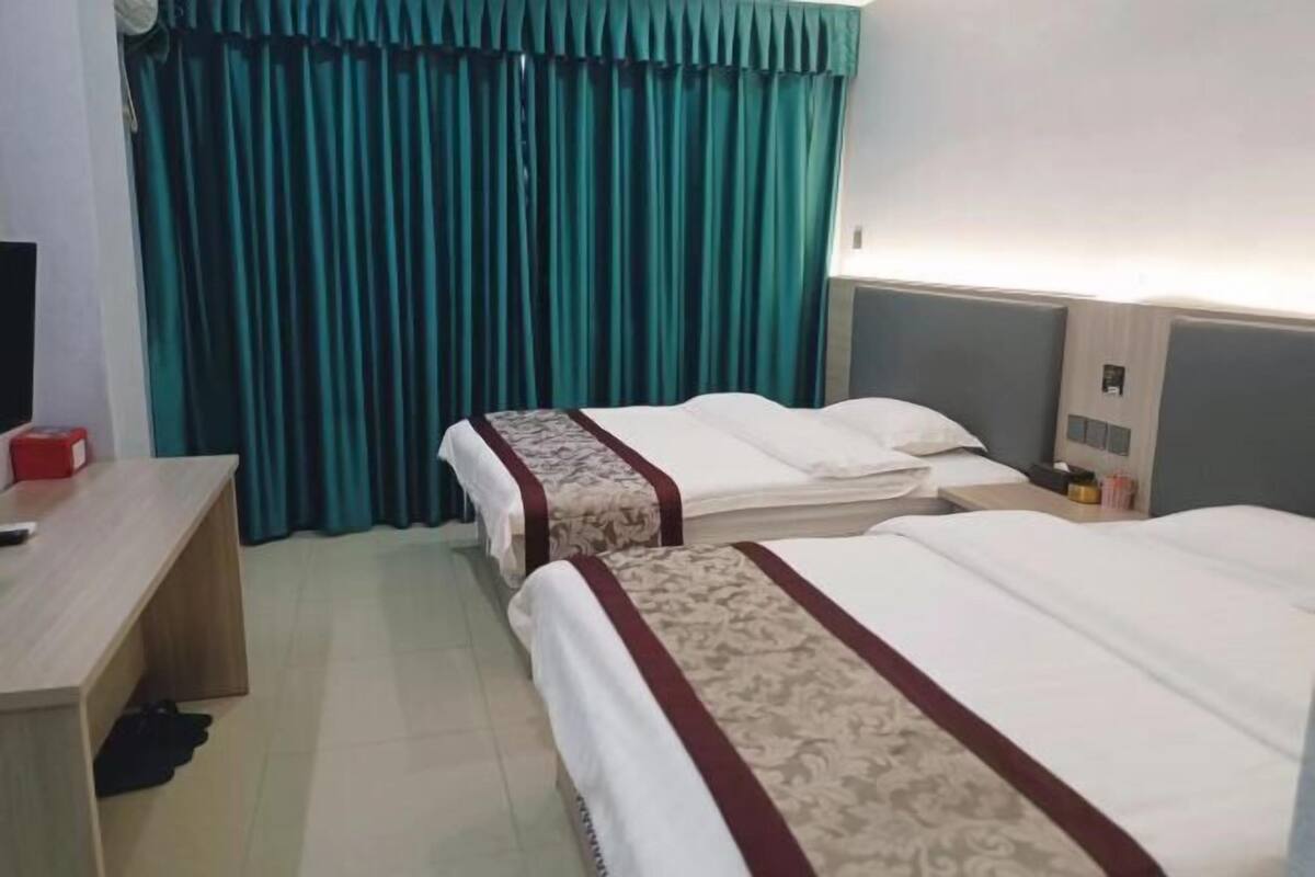 A hotel room with two beds, a desk, a TV, and teal curtains.