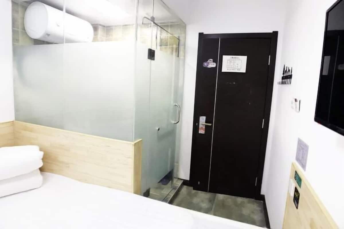 A hotel room with a bed, a glass shower enclosure, and a black door with a sign.