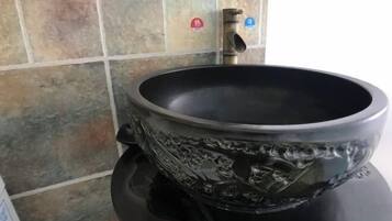 Un baño con un lavamanos de cerámica negra, un grifo y una pared con azulejos.