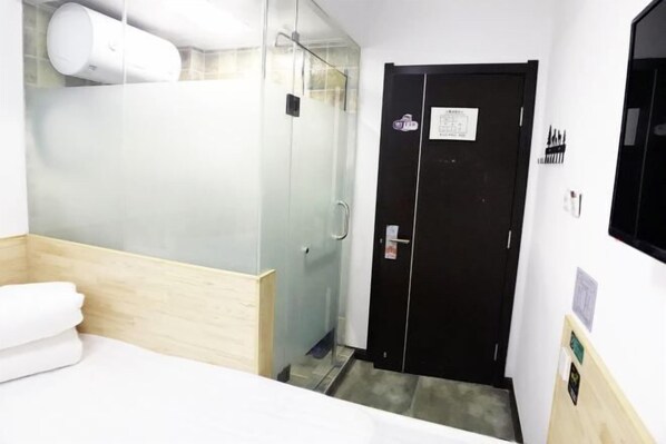 A hotel room with a shower, a bed, and a door with a sign. - Fushun ala warm hotel (Fushun)