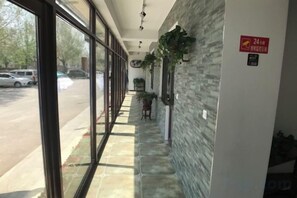 Un pasillo con pared de piedra, plantas en macetas y un letrero que indica zona de servicio las 24 horas.