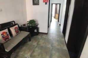 A hallway with a sofa, a plant, and a tiled floor.