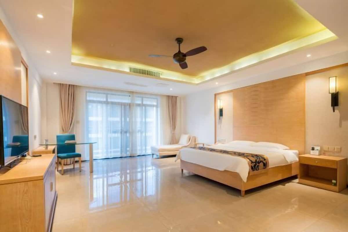 Una habitación de hotel moderna con una cama, un escritorio, una silla, un televisor y un ventilador de techo.
