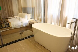 Een moderne hotelkamer met een groot bad, een opgemaakt bed en een nachtkastje met een telefoon.