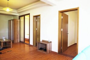 Een hotelkamer met houten vloer, een klein tafeltje, een schoenenrek en een deur naar een andere kamer.