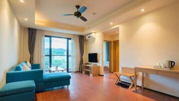A modern hotel room with a sofa, TV, desk, and a view of the outdoors.