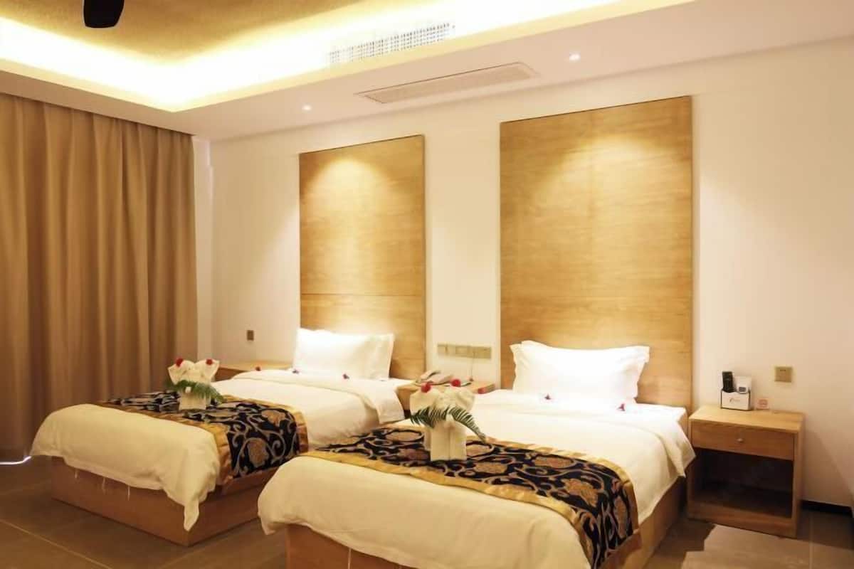 Habitación de hotel con dos camas, una mesita de noche y un ventanal con cortinas.