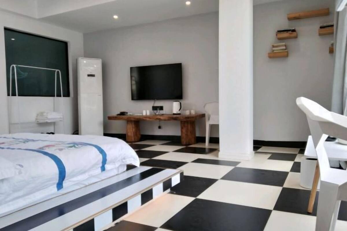 A modern bedroom with a bed, a desk, a television, and a chair.