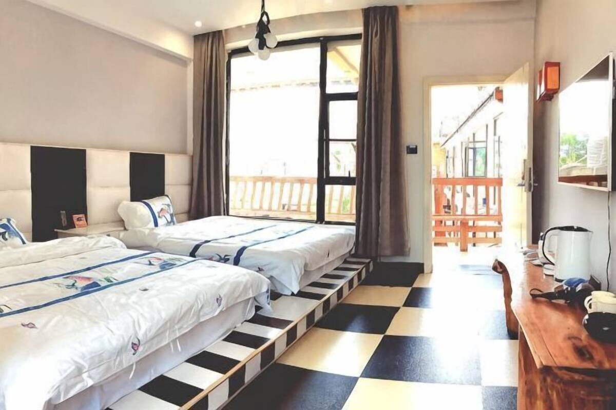 A hotel room with two beds, a checkered floor, a wooden bench, and a balcony with a railing.