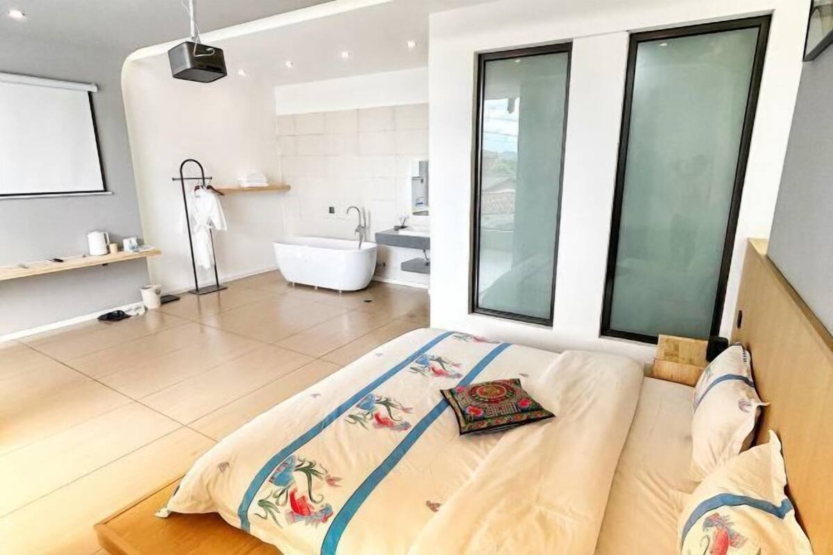 A modern bedroom with a large bed, a bedside table, a built-in bathtub, and a large window.