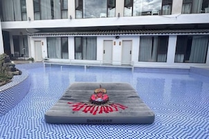 Área de piscina com cadeira de massagem e um edifício ao fundo.