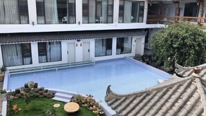 Un edificio tradicional con piscina en el patio, plantas en macetas y una valla de madera.