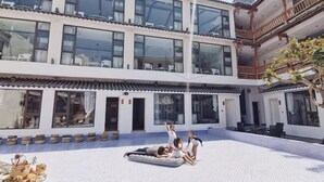 Un patio con piscina, un edificio con varios balcones y algunas personas relajándose.