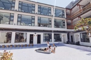 Un patio con piscina, un edificio con varios balcones y algunas personas relajándose.