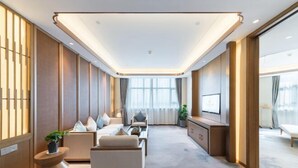 Een moderne hotelkamer met een bank, fauteuils, een televisie en een groot raam.