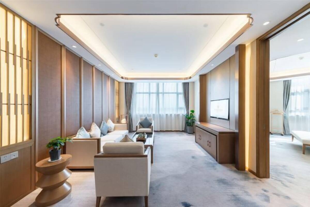 Een moderne hotelkamer met een bank, fauteuils, een televisie en een groot raam.