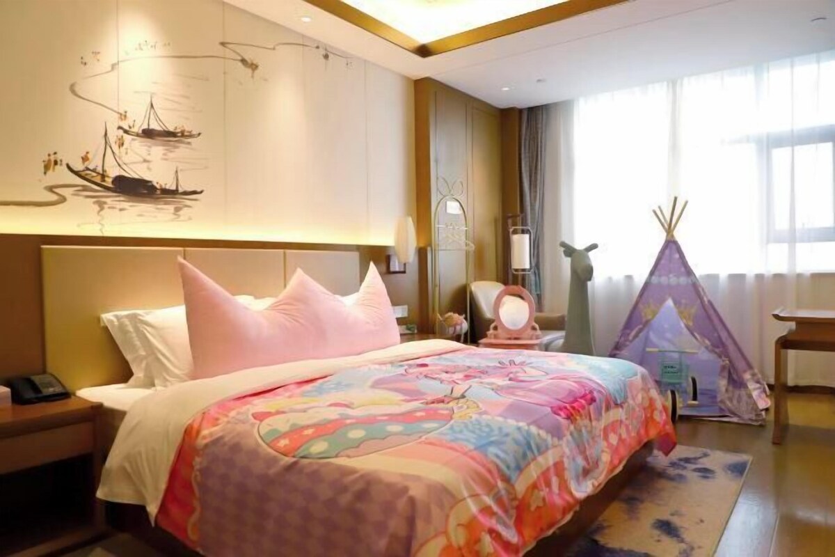 A hotel room with a bed, a nightstand, a wall with artwork, a window, and a teepee.