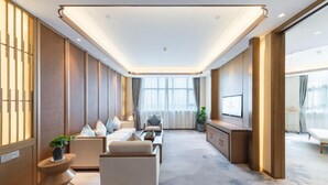 Een moderne hotelkamer met een bank, fauteuils, een televisie en een groot raam.