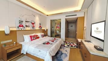 Una habitación de hotel moderna con cama, mesita de noche, televisor y un escritorio pequeño.