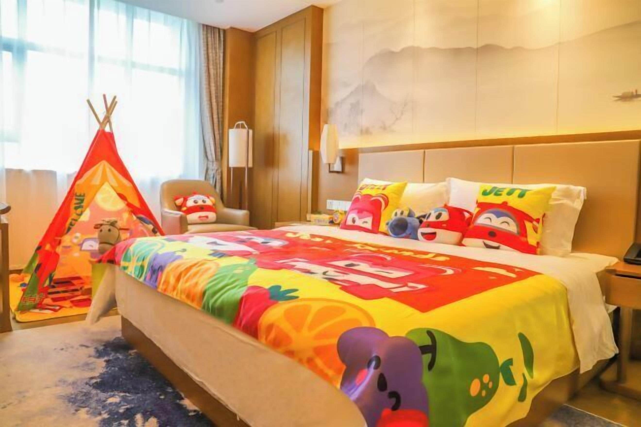 Habitación de hotel con cama, una silla, una mesita, ventana con cortinas y una lámpara de pared.