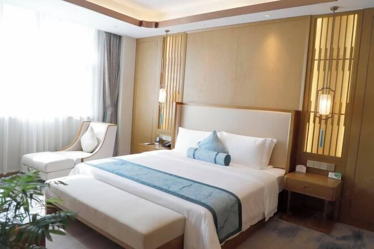Een hotelkamer met een groot bed, een nachtkastje, een stoel en een raam met gordijnen.