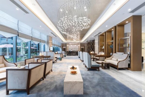 A spacious hotel lobby with a central marble coffee table, seating areas, and a modern chandelier.