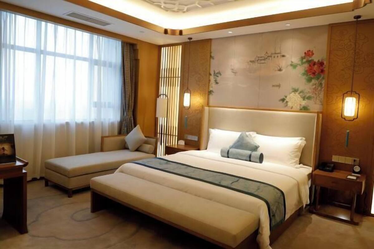 Hotelkamer met een groot bed, een kleinere sofa, een bureau en een raam met gordijnen.