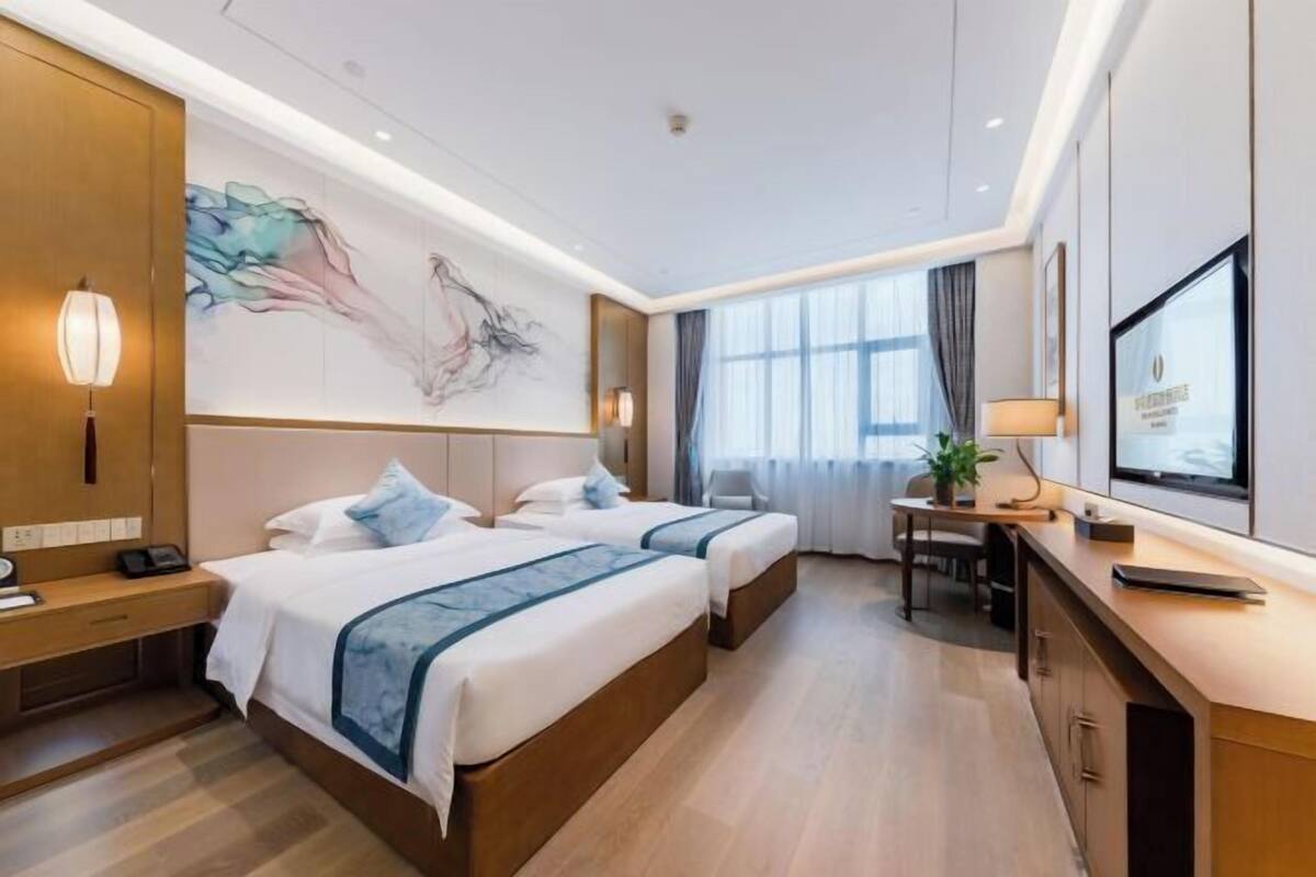 Een hotelkamer met twee bedden, een bureau, een stoel en een groot raam.