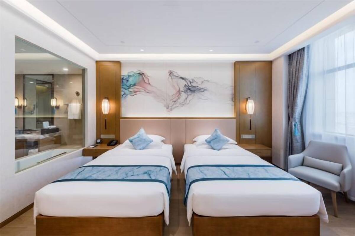 Een hotelkamer met twee bedden, een grote spiegel, een schilderij aan de muur en een stoel.